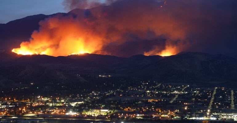 Massive wildfire in the foothills of a city at dusk.