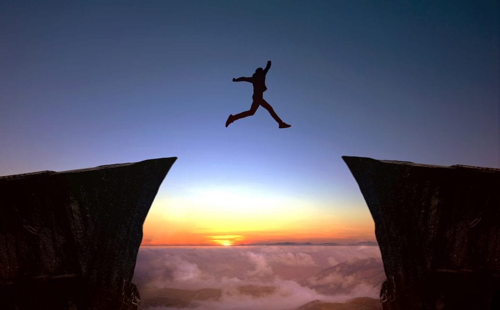 photo depicting the person who focuses on the target while leaping between two cliffs in silhouette against a sunset.