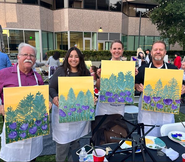 Duthie Power employees Corinne Rodriguez, Peter Thornton, Mike Goodman and Vanessa Marquez holding paints of green trees and purple flowers